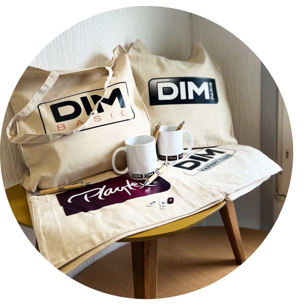 Opération DIM : totebags en coton naturel DIM Basic, DIM Paris, Playtex et DIM Expert Care; Mugs blancs en céramique avec sublimation all over DIM Paris et Playtex; Stylos en bambou DIM Basic, Playtex, DIM Paris et DIM Expert Care; et cache-webcams blancs et noirs DIM Paris, DIM Expert Care et Playtex